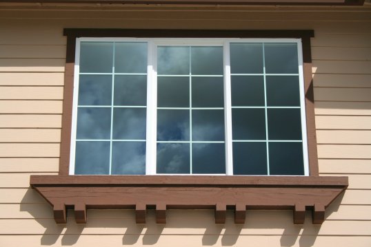 A window with brown wood trim and the beige exterior of a house
