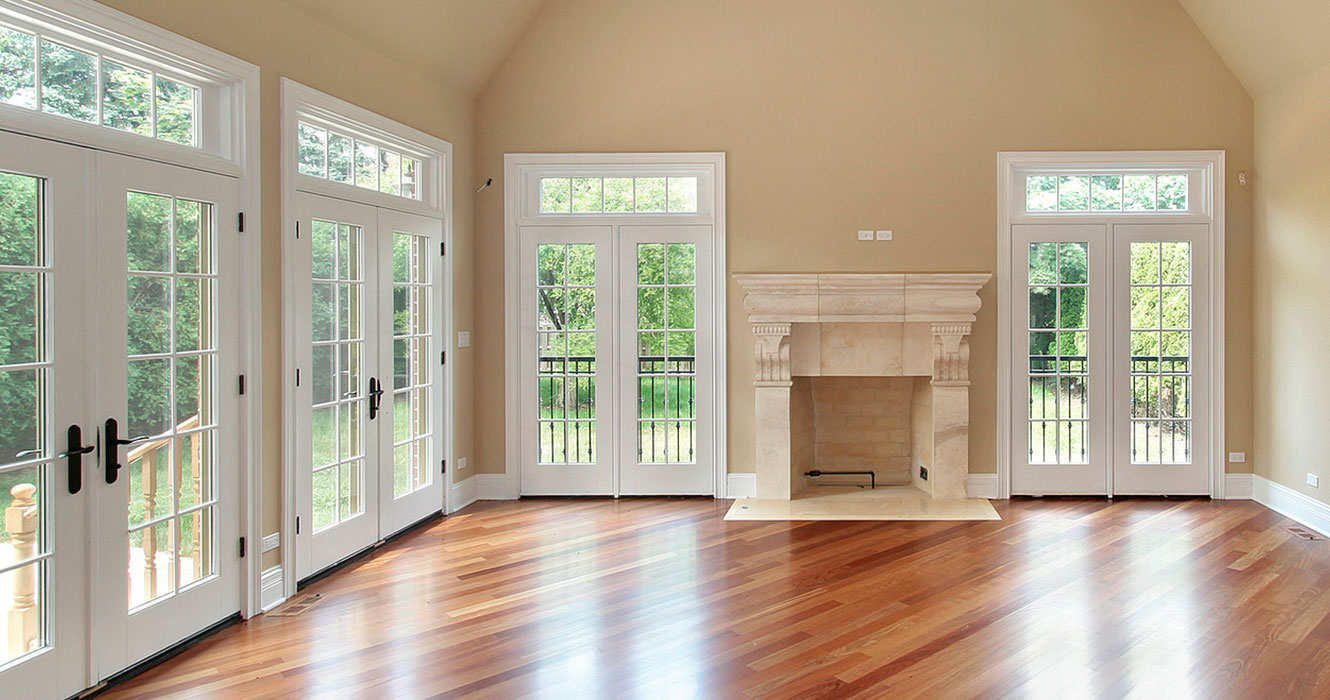 Empty living room with two sets of white French doors on left side, leading to forested yard.