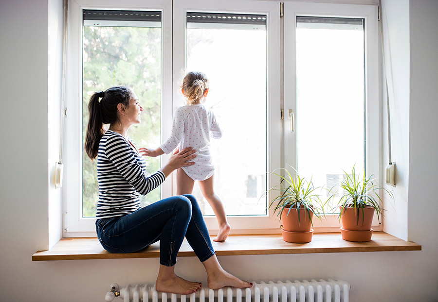 A mom holding a child on a thick window sill as she looks out the windows