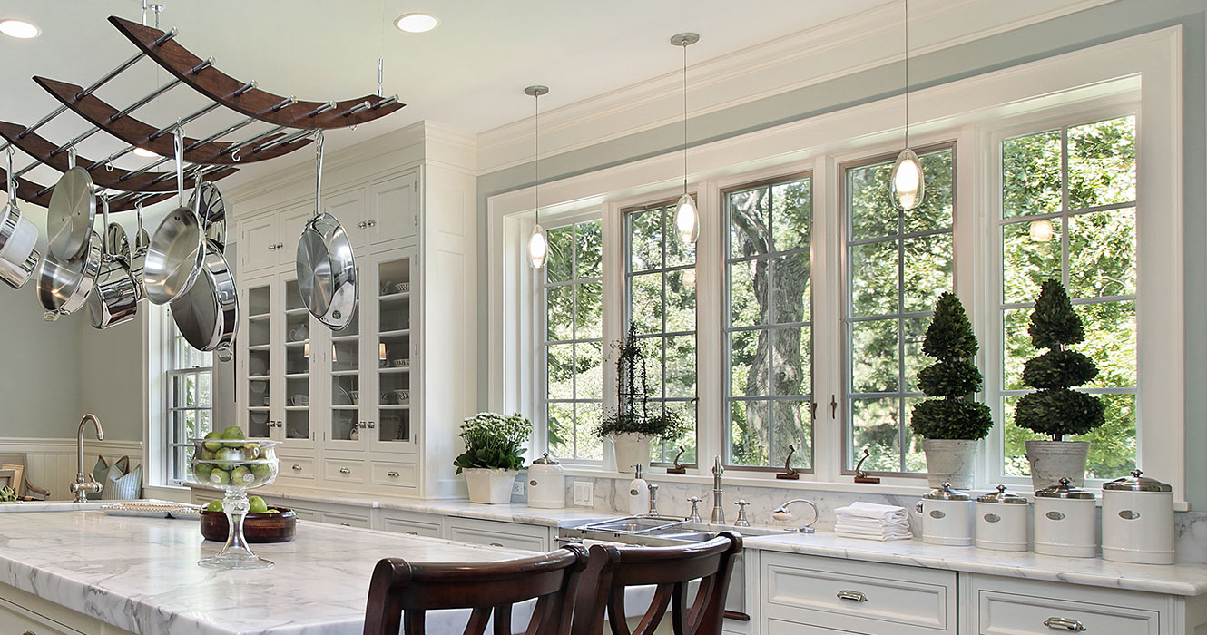 Large white kitchen with island and row of white casement windows with grids above kitchen sink.
