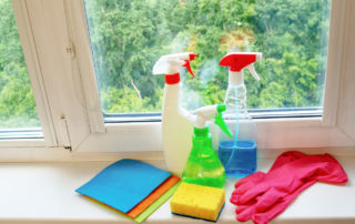 Window cleaning products are located on the windowsill - spray guns, rubber gloves, a sponge and rags