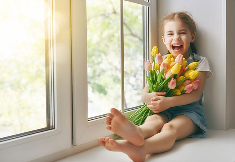 Young girl sitting by window hugging a bundle of tulips